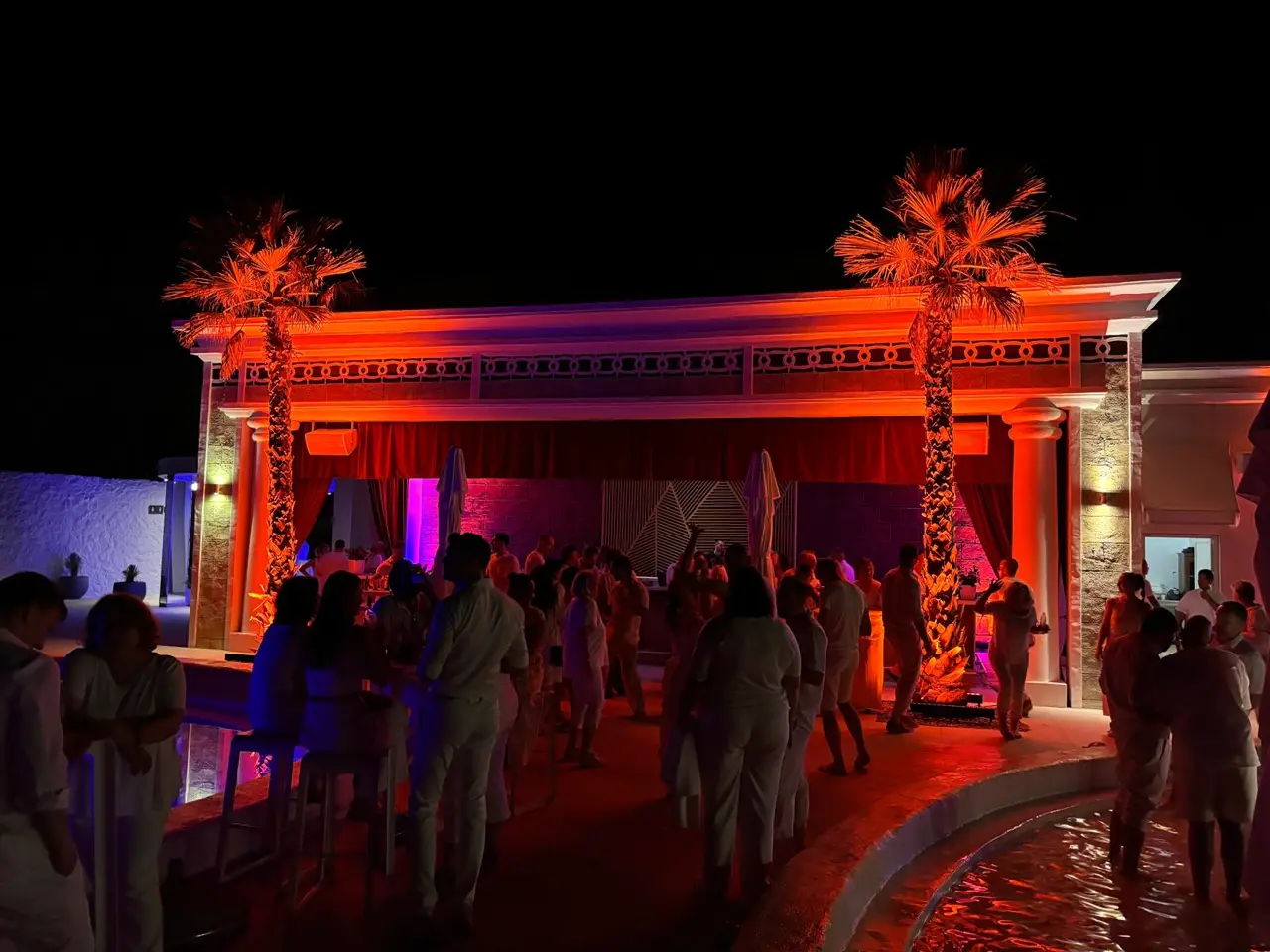 Gosti uživaju u korporativnoj zabavi uz bazen u En Vogue Beach Clubu u Šibeniku, s profesionalnom, višebojnom rasvjetom za događaje s toplim narančastim i hladnim plavo/ljubičastim zonama.